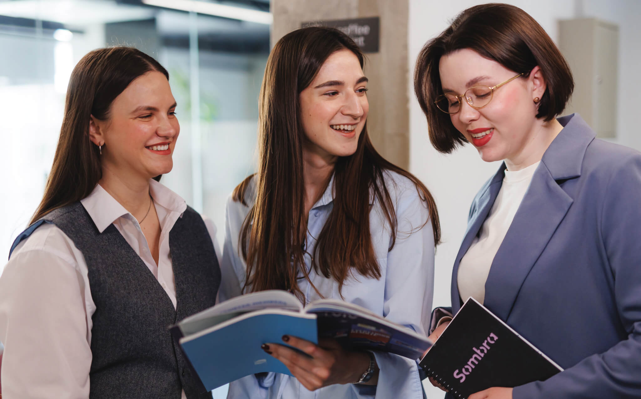 Three women in a lively discussion holding notebooks, representing open and inclusive communication at Sombra.