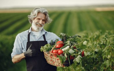 Smiling farmer holding a basket of fresh vegetables in a cultivated field, symbolizing data-driven agricultural success.