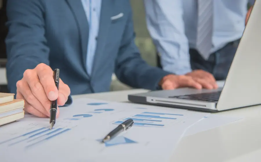 A photo showing people's hands working on a laptop and reviwing reports